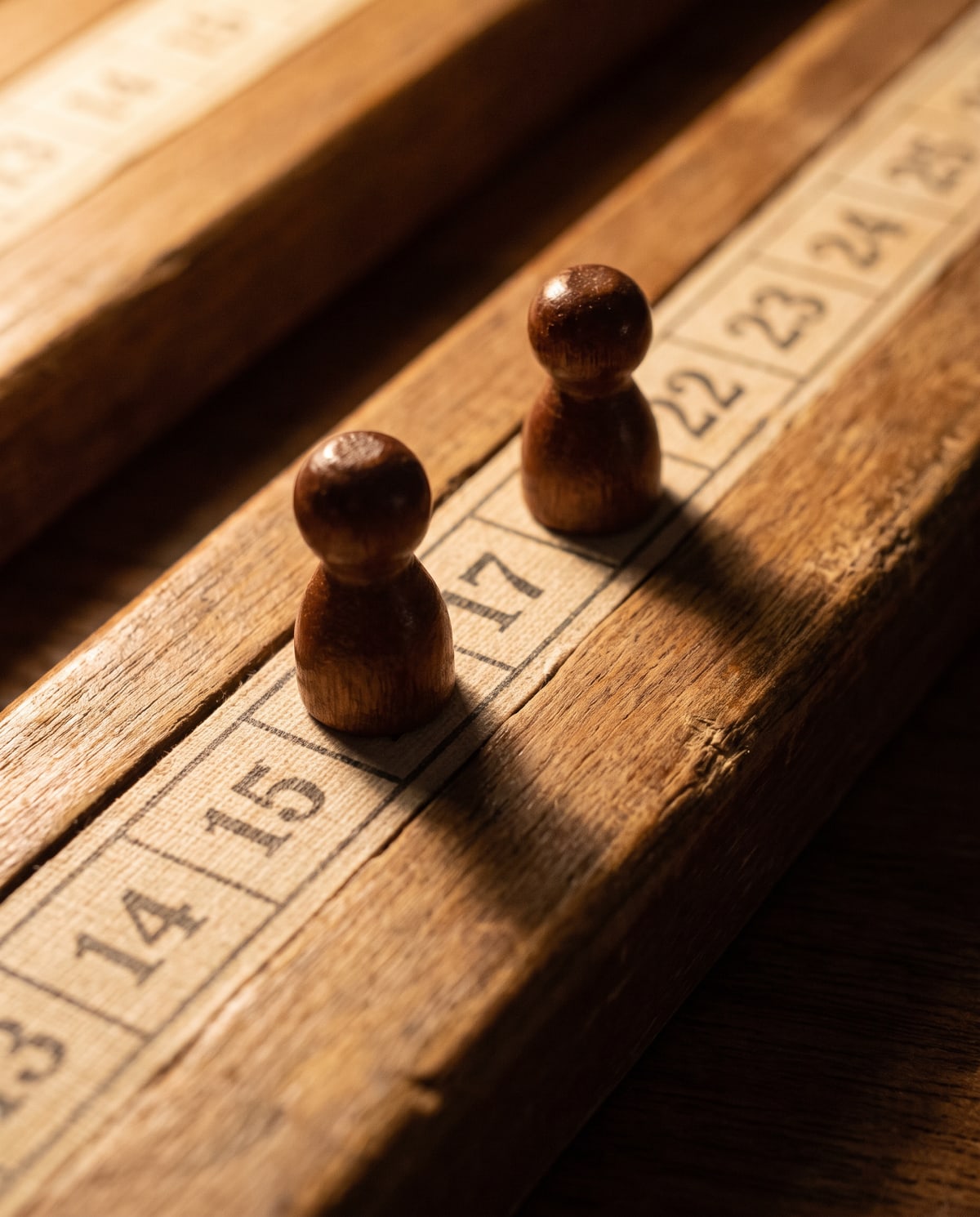 A scoring track photographed close: a line of small numbered squares with two wooden markers standing on it, one several spaces ahead of the other