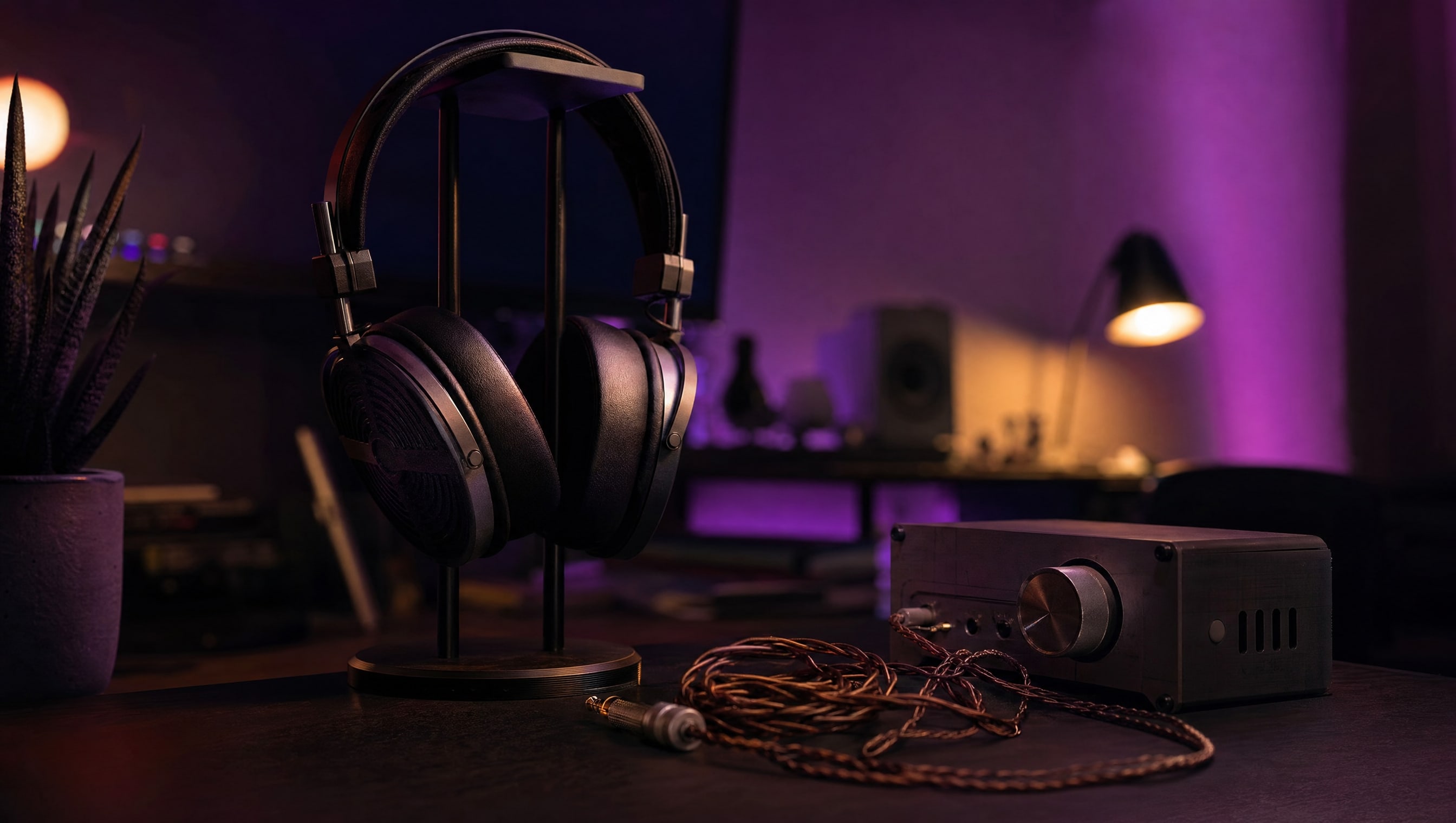 A desk at night: headphones on a stand, a coiled cable, a small amplifier with one knob.