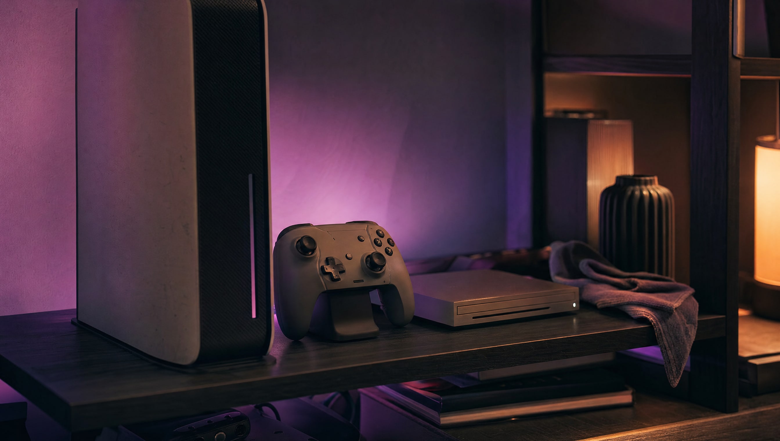 A shelf at night: an upright console, a controller on a stand, a slim drive and a cloth.
