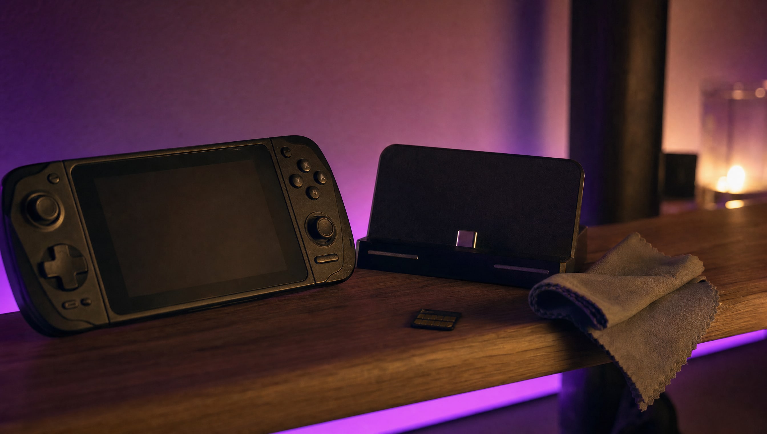 A shelf at night: a handheld, its dock, a memory card and a cleaning cloth.