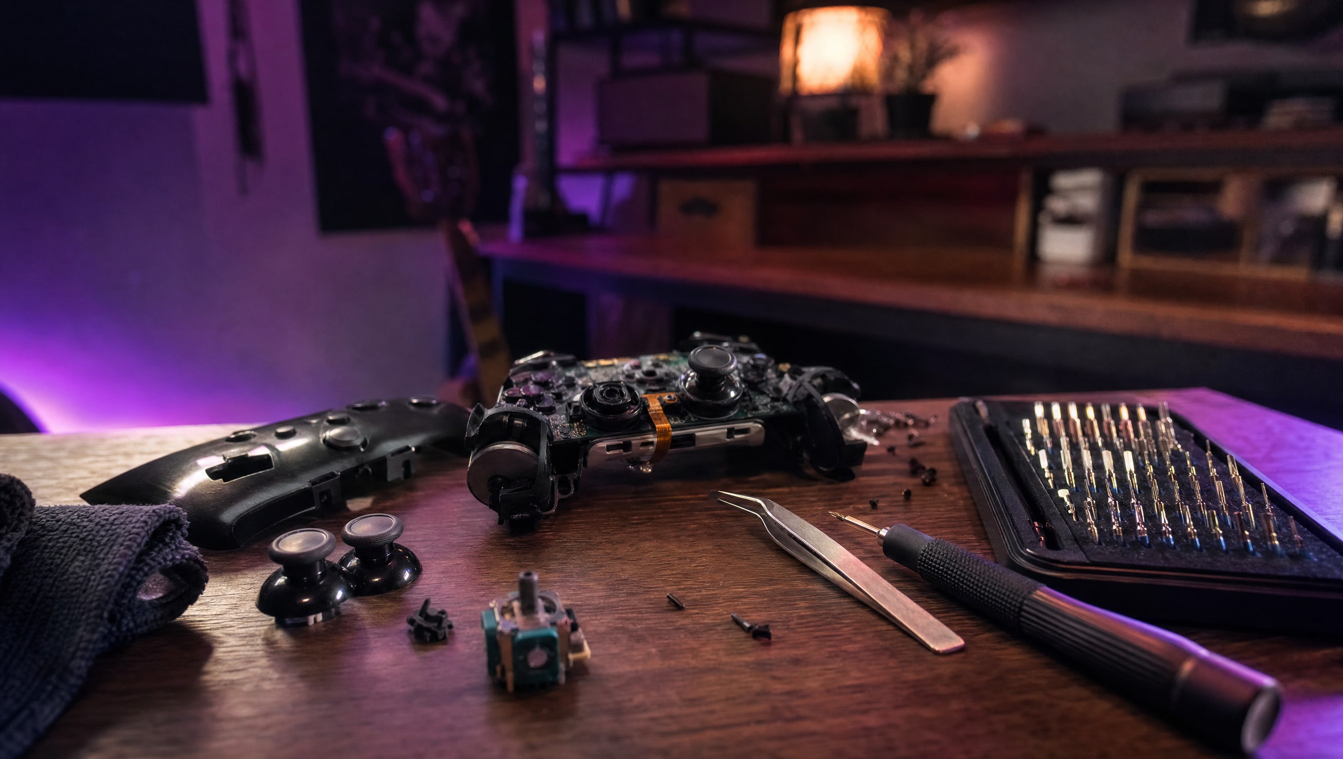 A workbench at night: a controller in pieces, a screwdriver set, tweezers and a stick module.