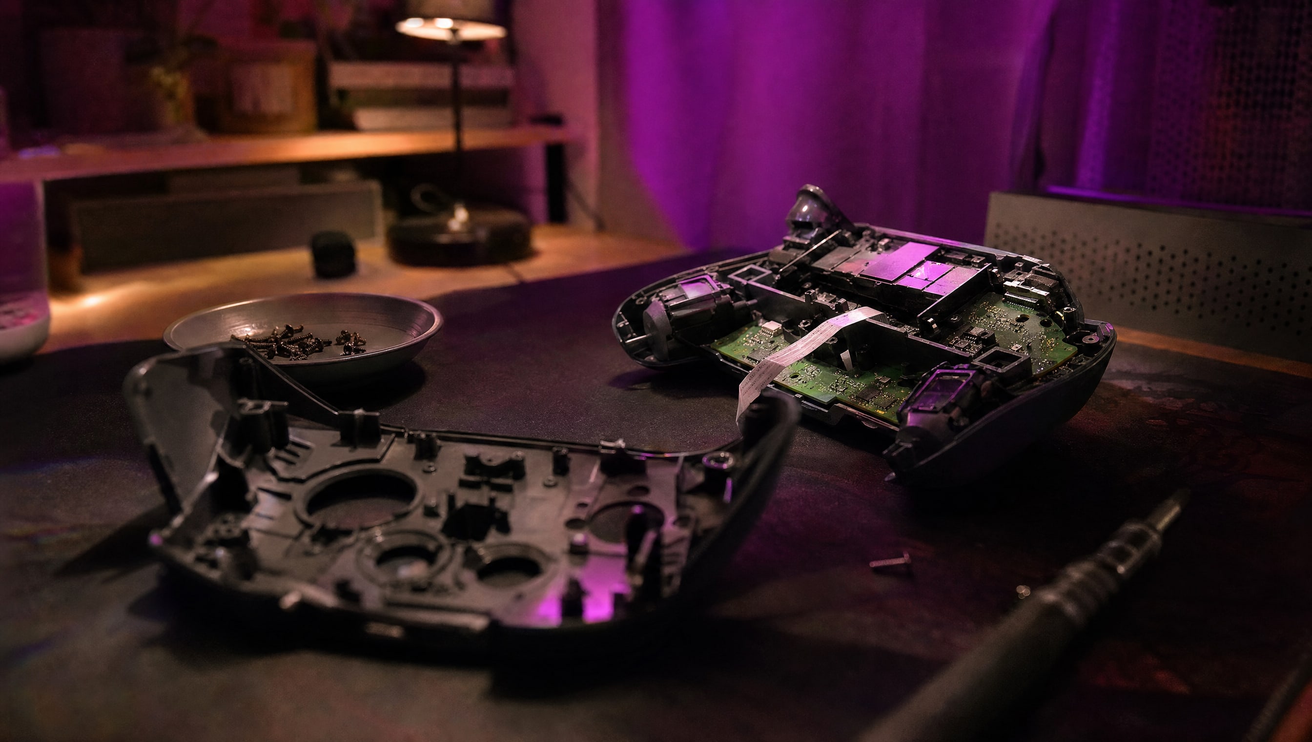A controller face down and opened, its shell in two halves, screws in a dish.
