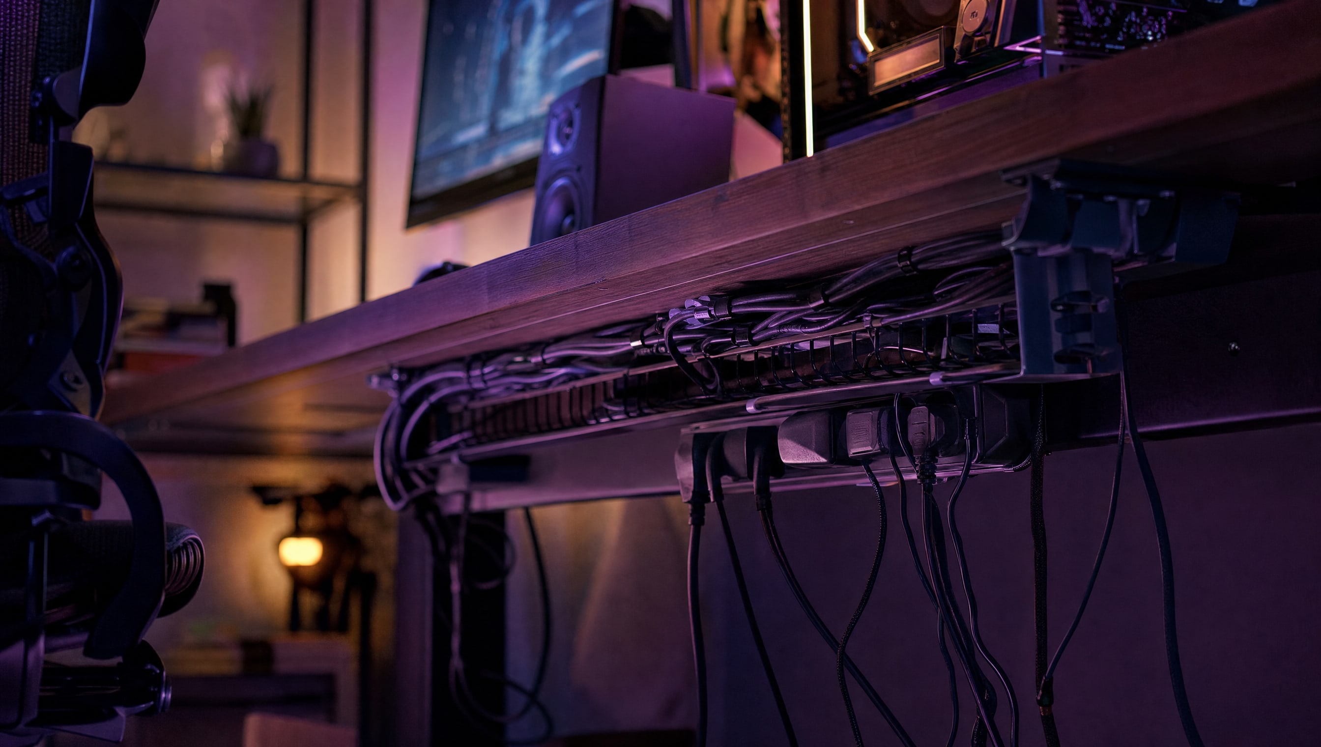 A desk at night: a cable tray under the surface, a loom running into it, a power strip.