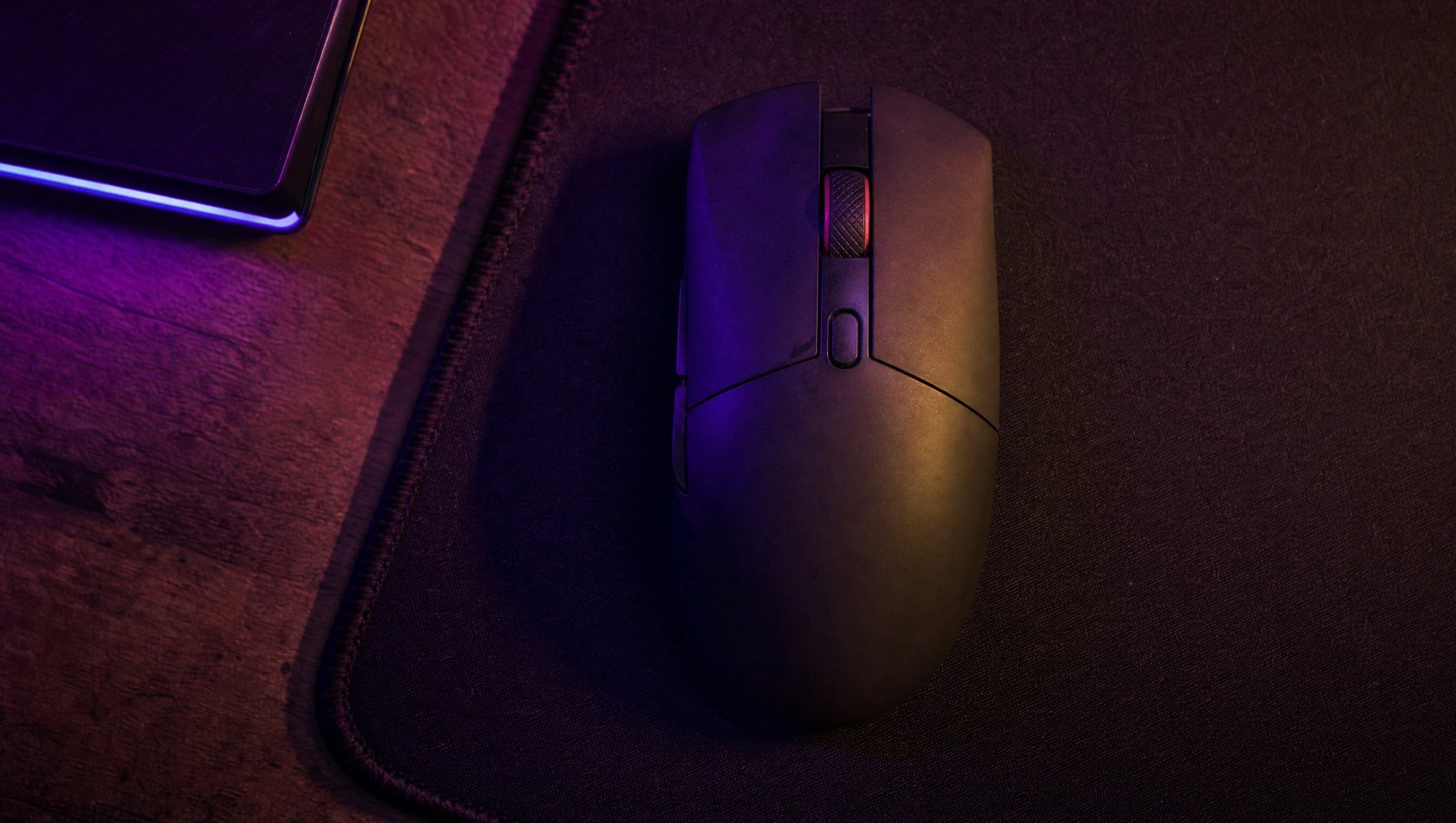 A gaming mouse from directly above on a cloth pad, its shell shape and button split readable.