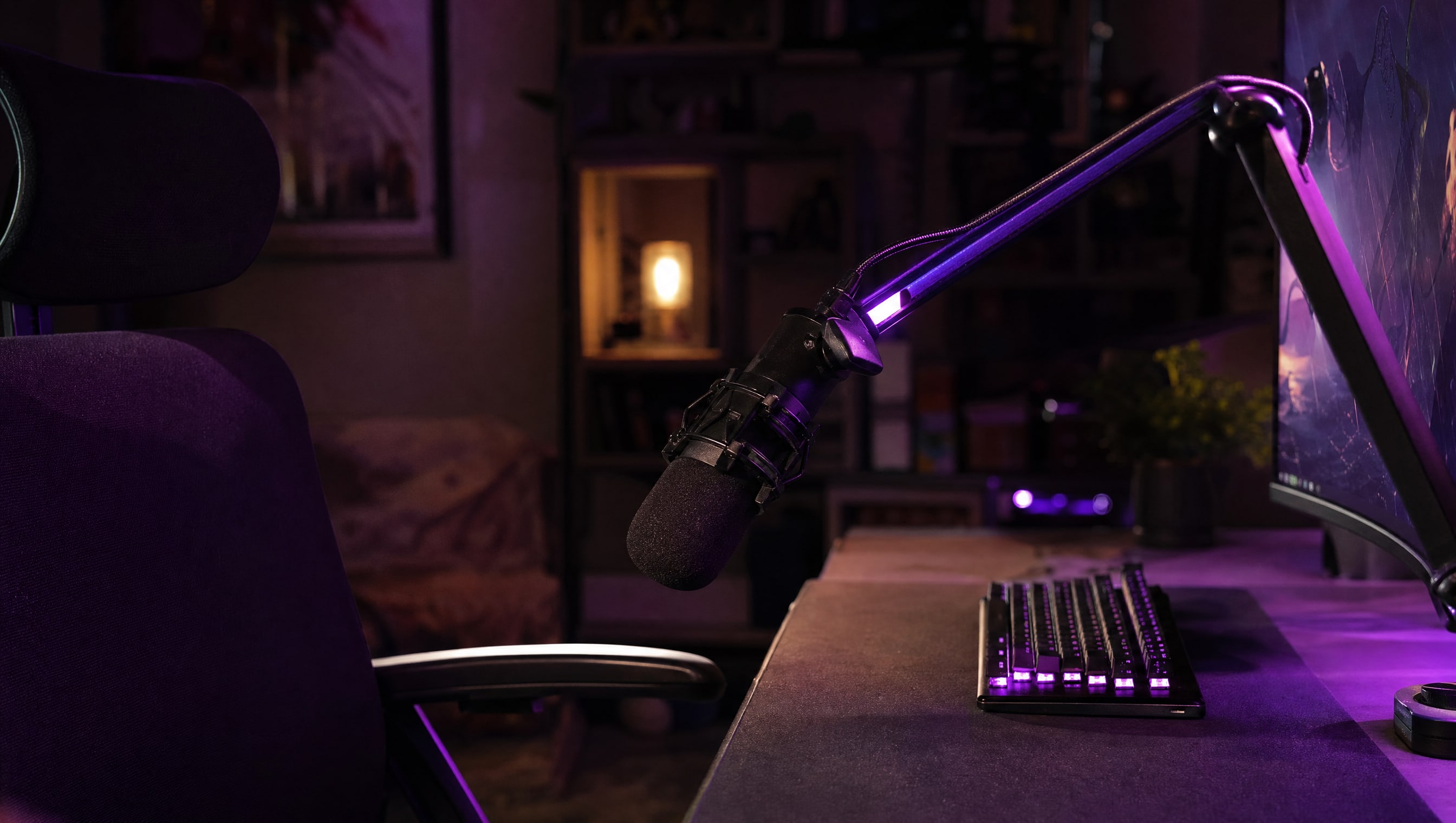 A microphone on a low desk arm angled down toward a chair, a keyboard behind it and out of its line.