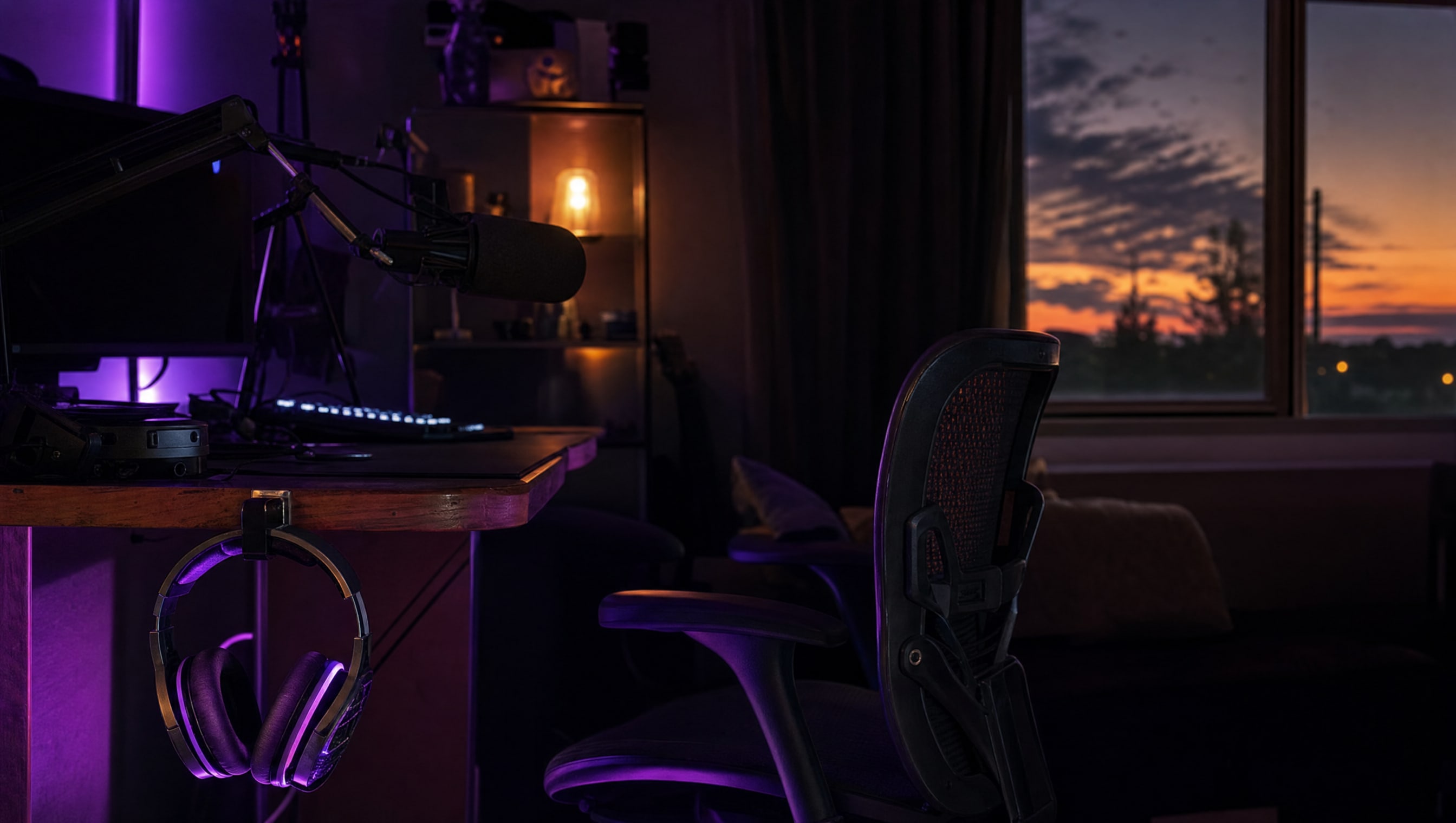 Over-ear headphones hanging from a hook at the left edge of a desk, a boom microphone behind them.