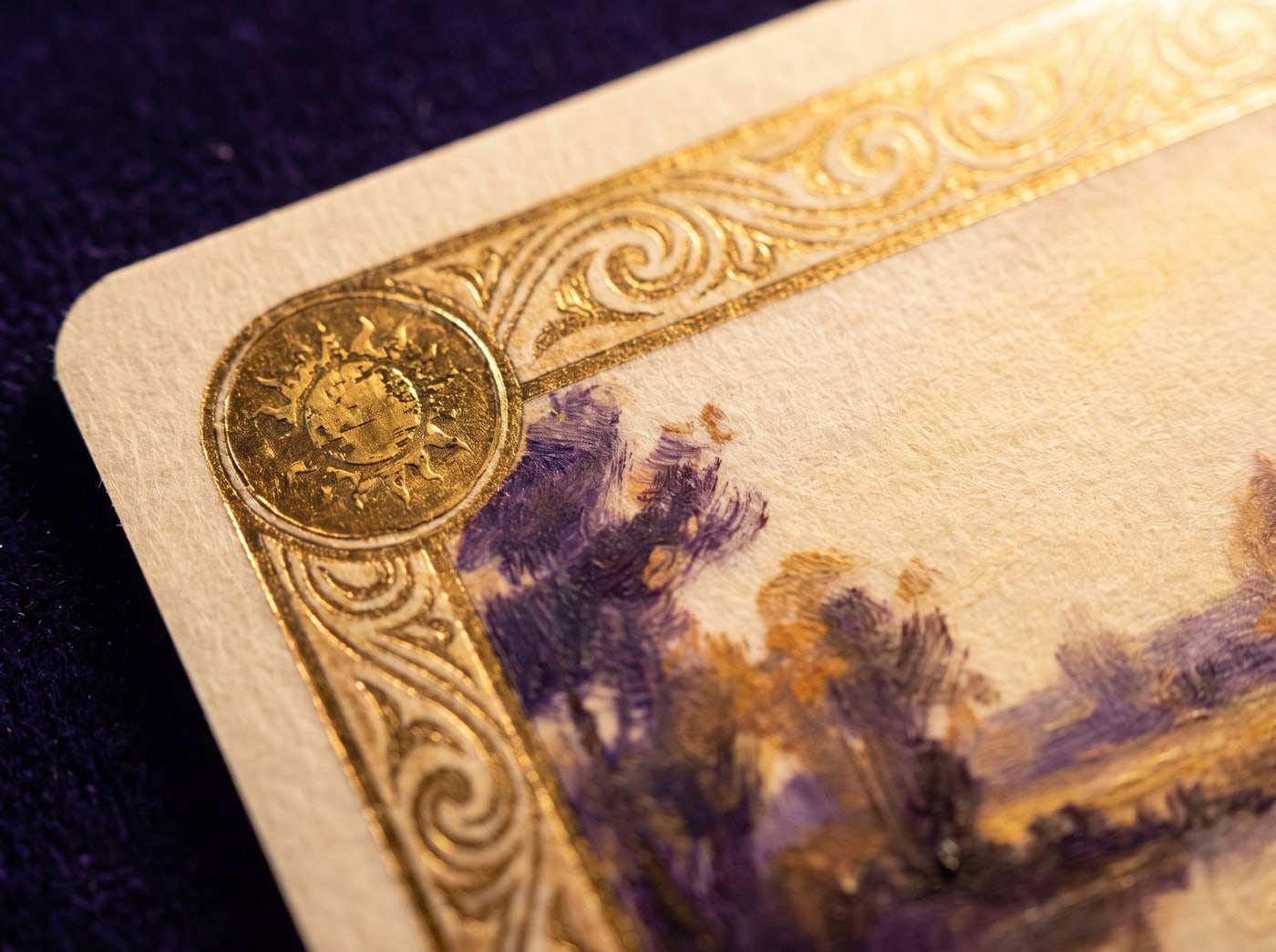 Extreme macro of a card corner: engraved gilt border, a circular cost medallion, the edge of a painted landscape.