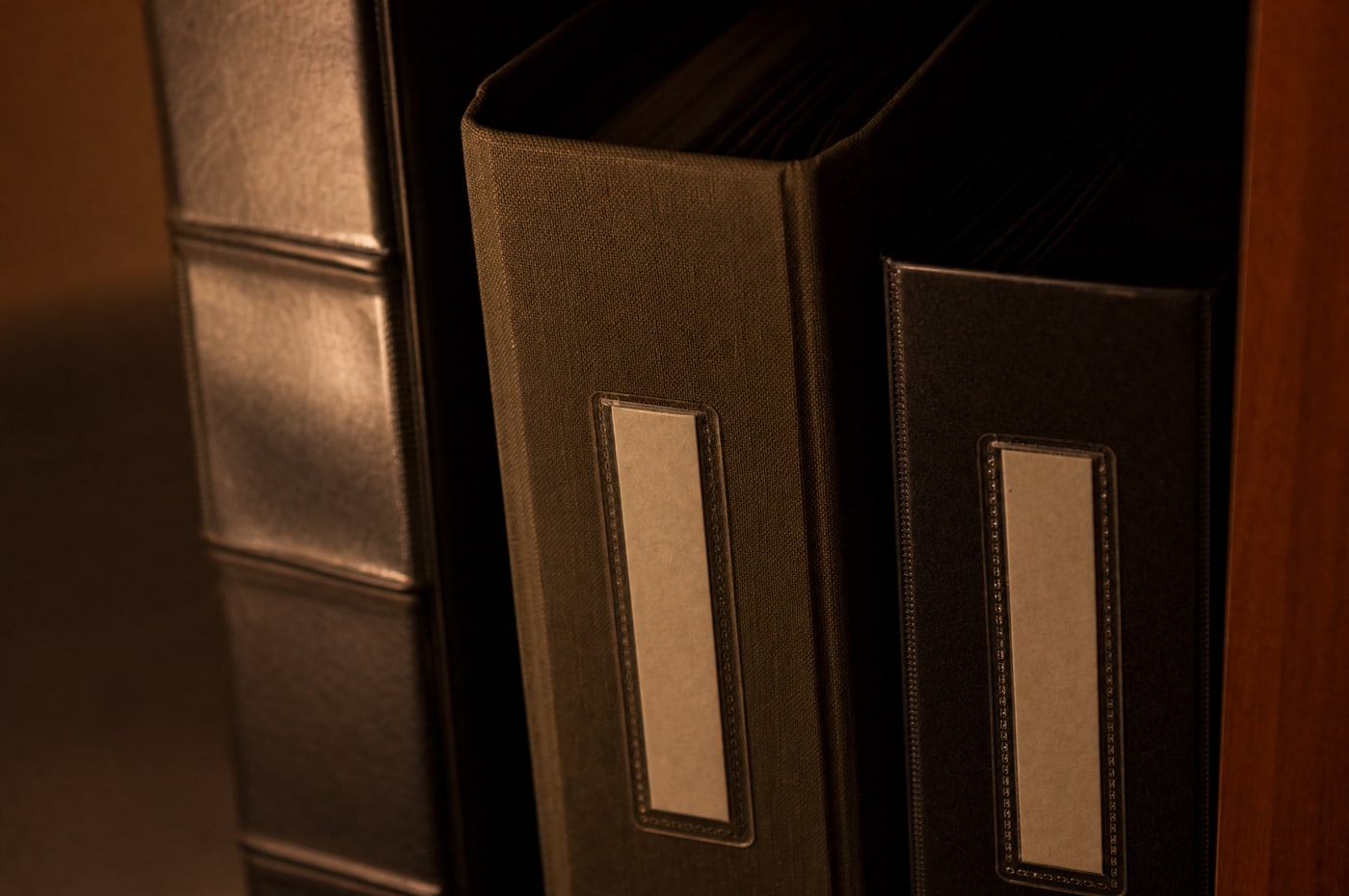 A close view of a binder spine standing on a shelf between two others, cloth and board texture, its label strip carrying no text.