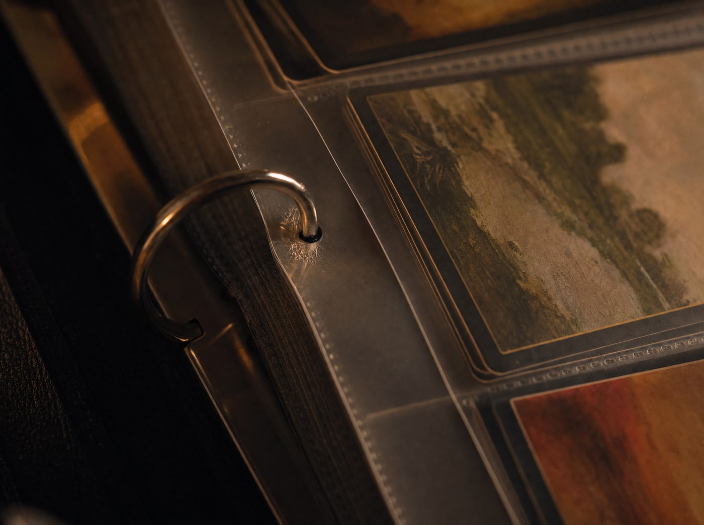 The open metal ring mechanism of a binder, one ring passing through a page hole, the page slightly stressed around it.