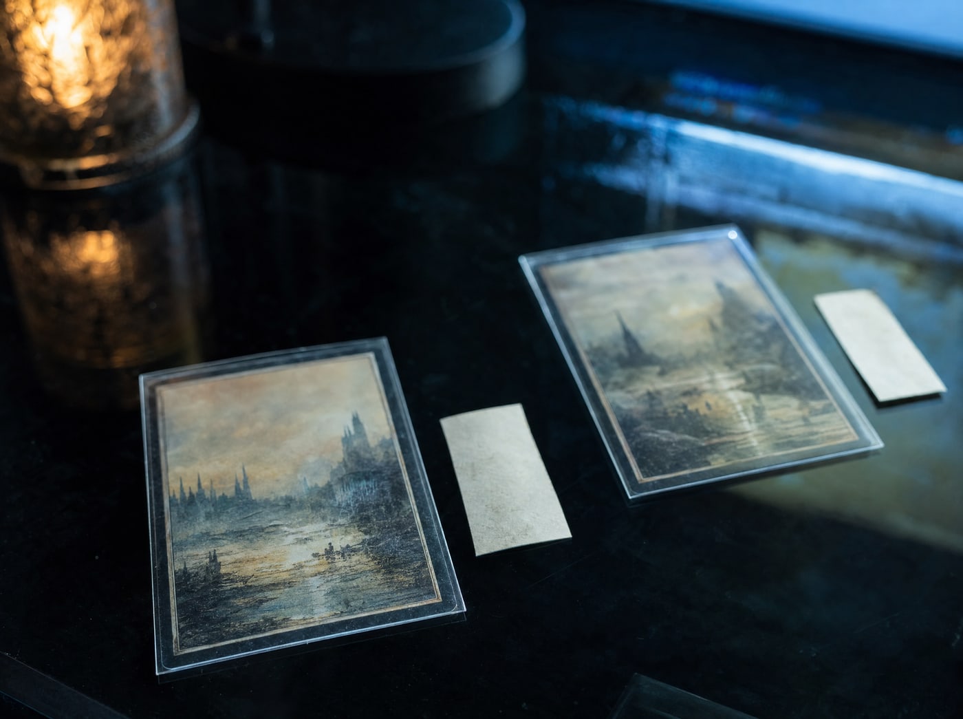 Two identical sleeved cards laid a hand apart on dark glass, each with a small paper slip beside it.