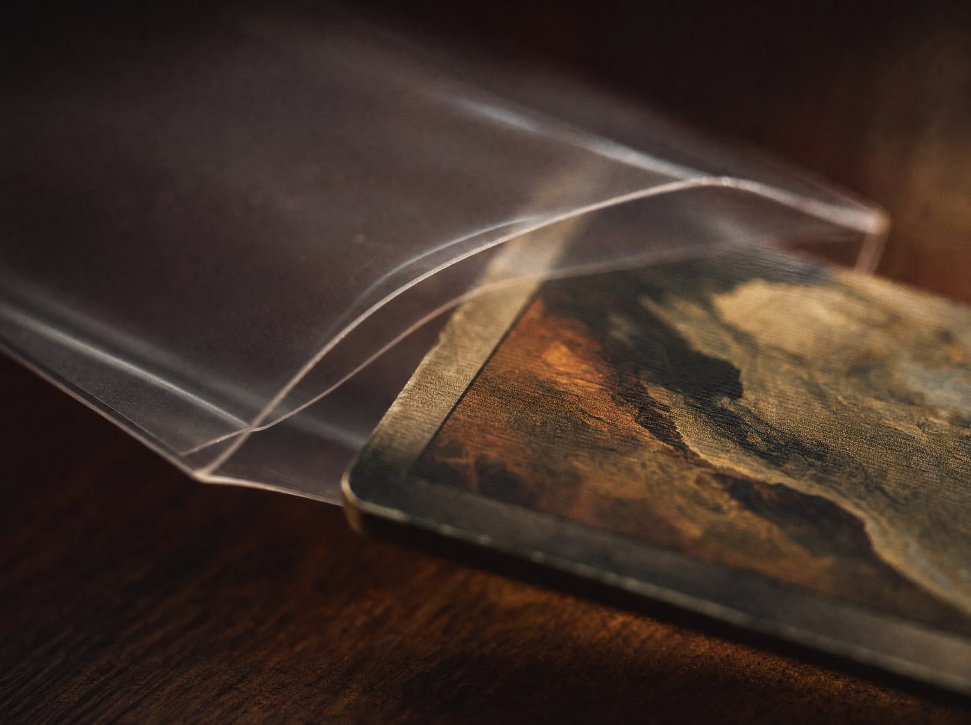 Extreme macro on the open mouth of a card sleeve, the thin polypropylene lip catching lamplight as a card edge enters it.